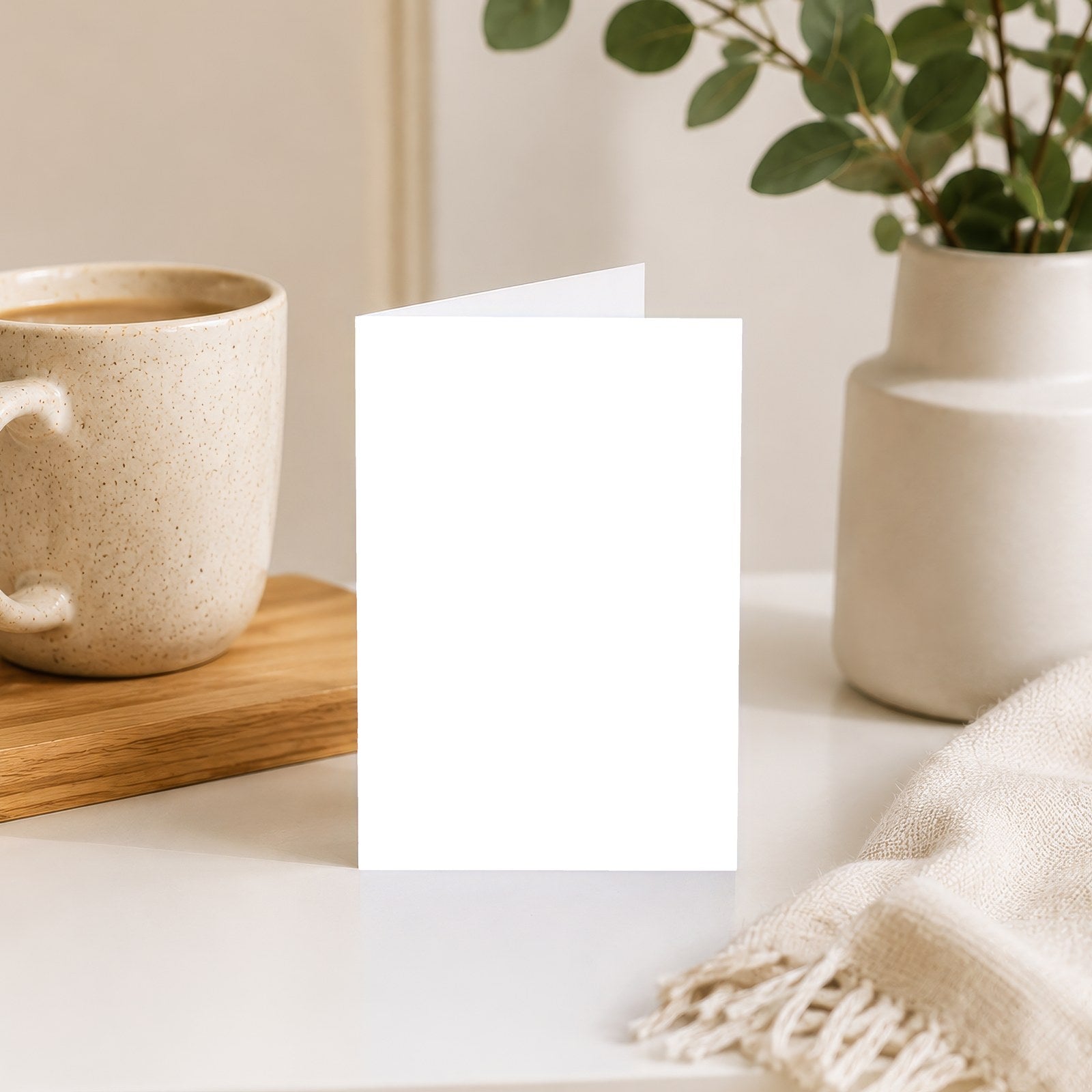 Greeting card standing on a desk beside a mug and a vase of eucalyptus