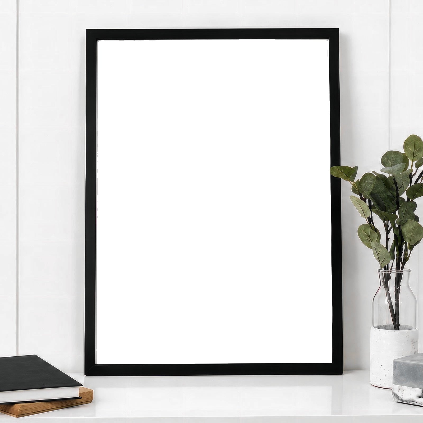 Black framed print with a white matte leaning on a shelf beside eucalyptus and books
